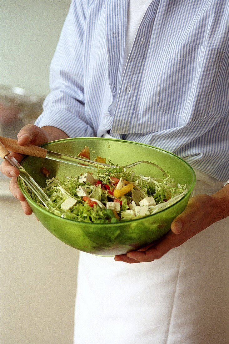 Man holding a dish of mixed salad with sheep's cheese