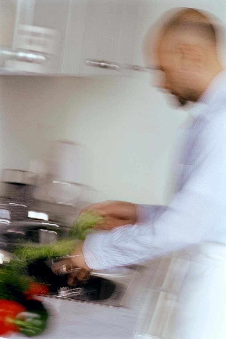 Mann wäscht Gemüse und Salat im Küchespülbecken