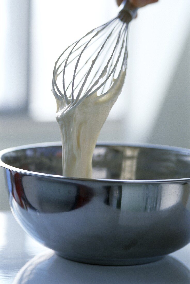 Egg whisk with sponge mix over a metal bowl
