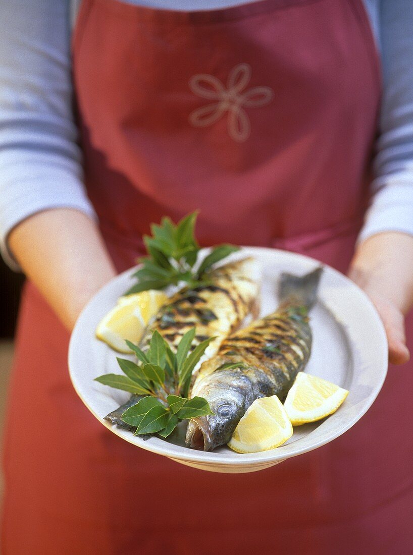 Woman holding platter of sea bass with bay leaves