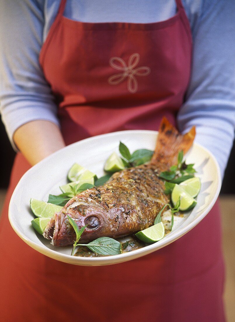 Frau hält Platte mit gegrilltem Red Snapper