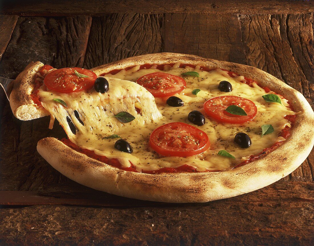 Pizza Margherita auf Holzuntergrund, Stück auf Pizzaheber