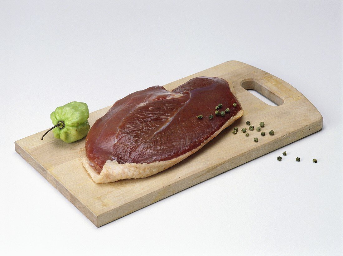 Duck breast on wooden board with peppercorns and peppers