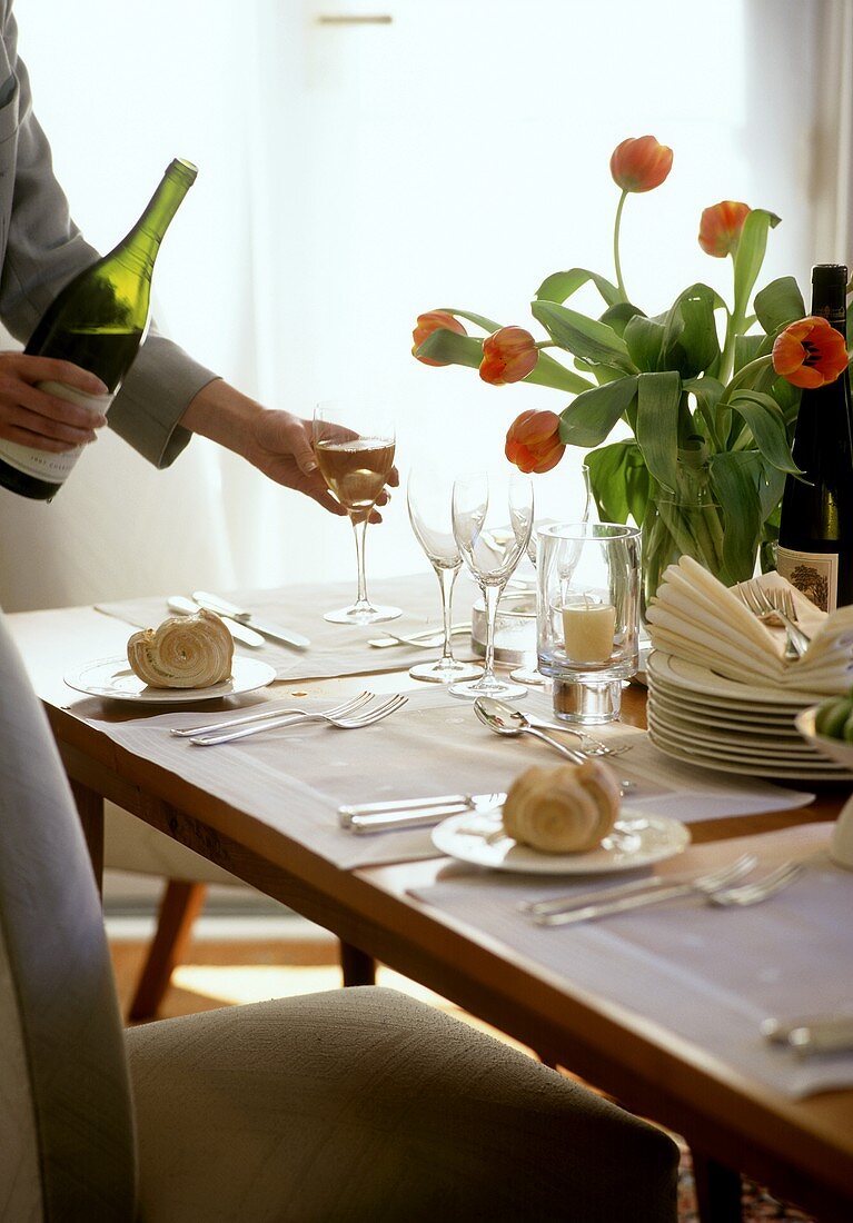 Wein wird eingeschenkt an stilvoll gedecktem Tisch mit Tulpen