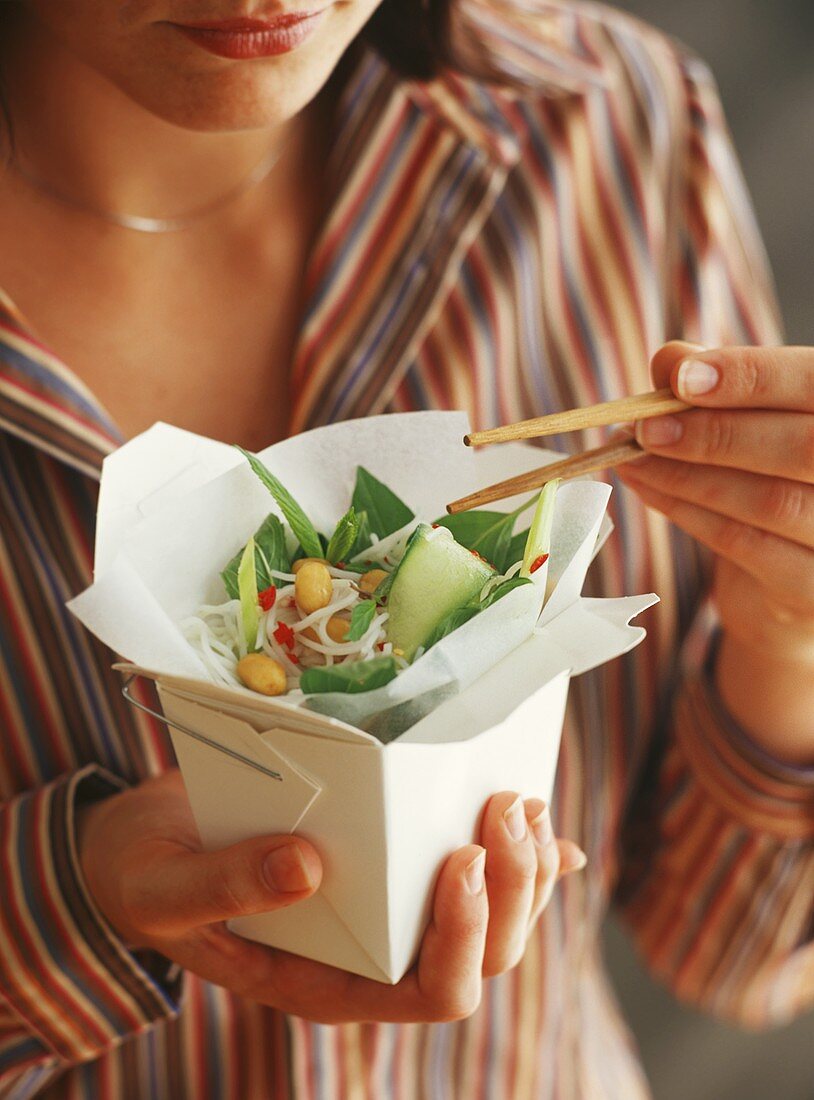 Frau hält Take-away-Behälter mit asiatischem Reisnudelsalat