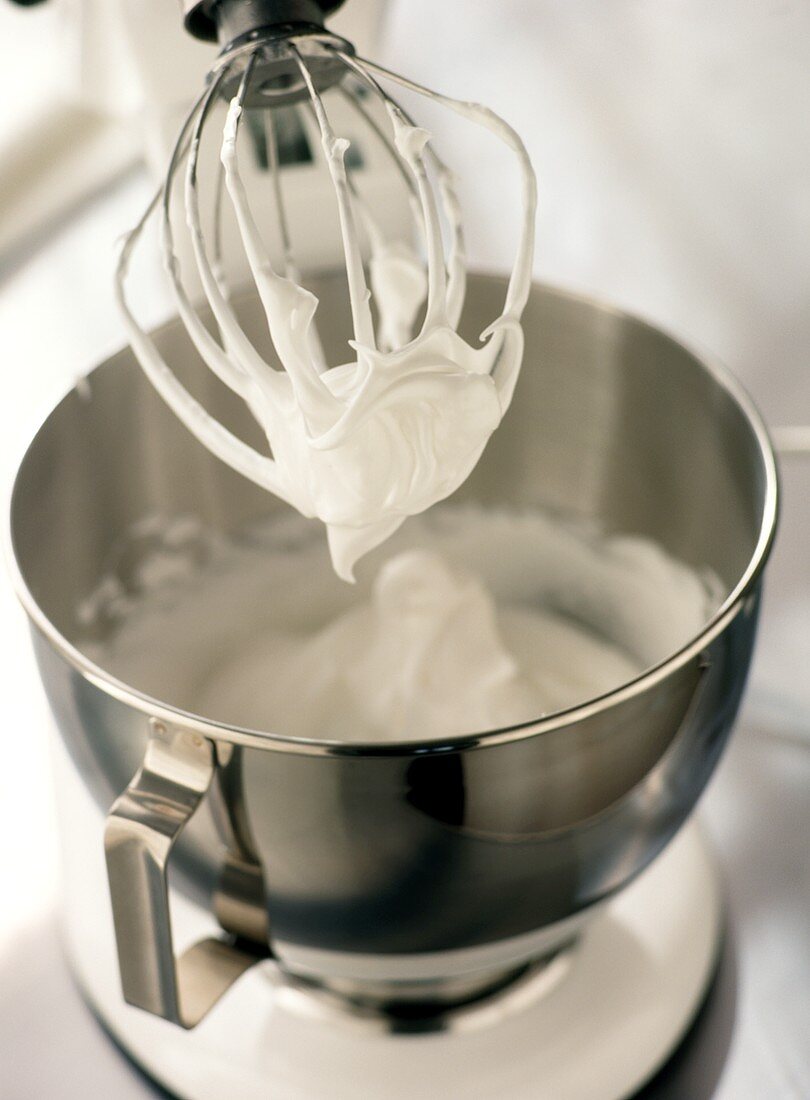 Beaten egg white in a bowl and on whisk