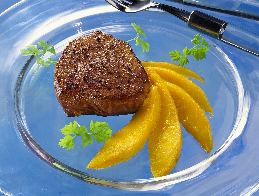 Peppered steak with mango wedges on glass plate