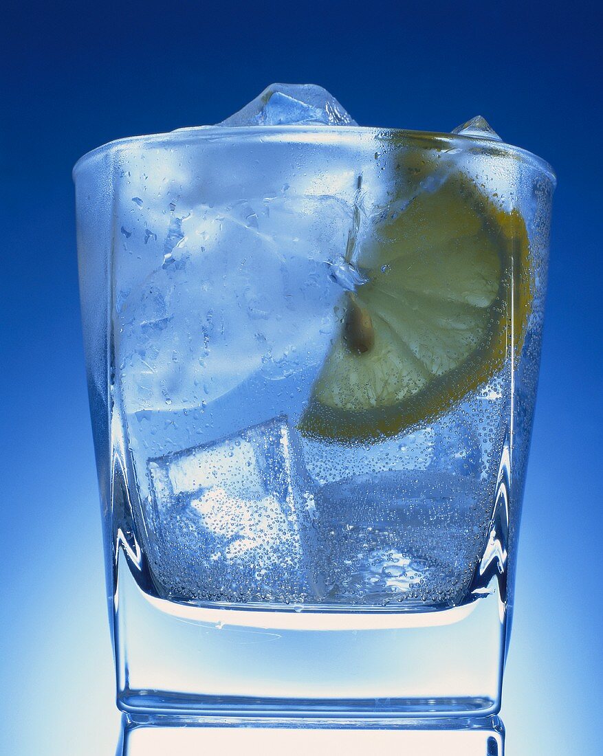Glas Gin Tonic mit Eis & Zitrone vor blauem Hintergrund