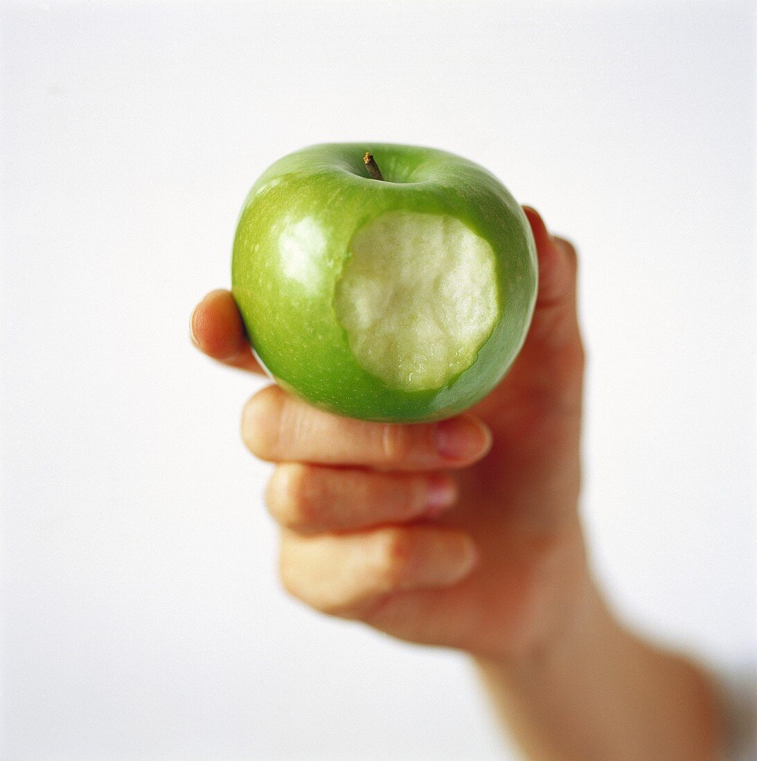 Hand holding a green apple with a bite taken