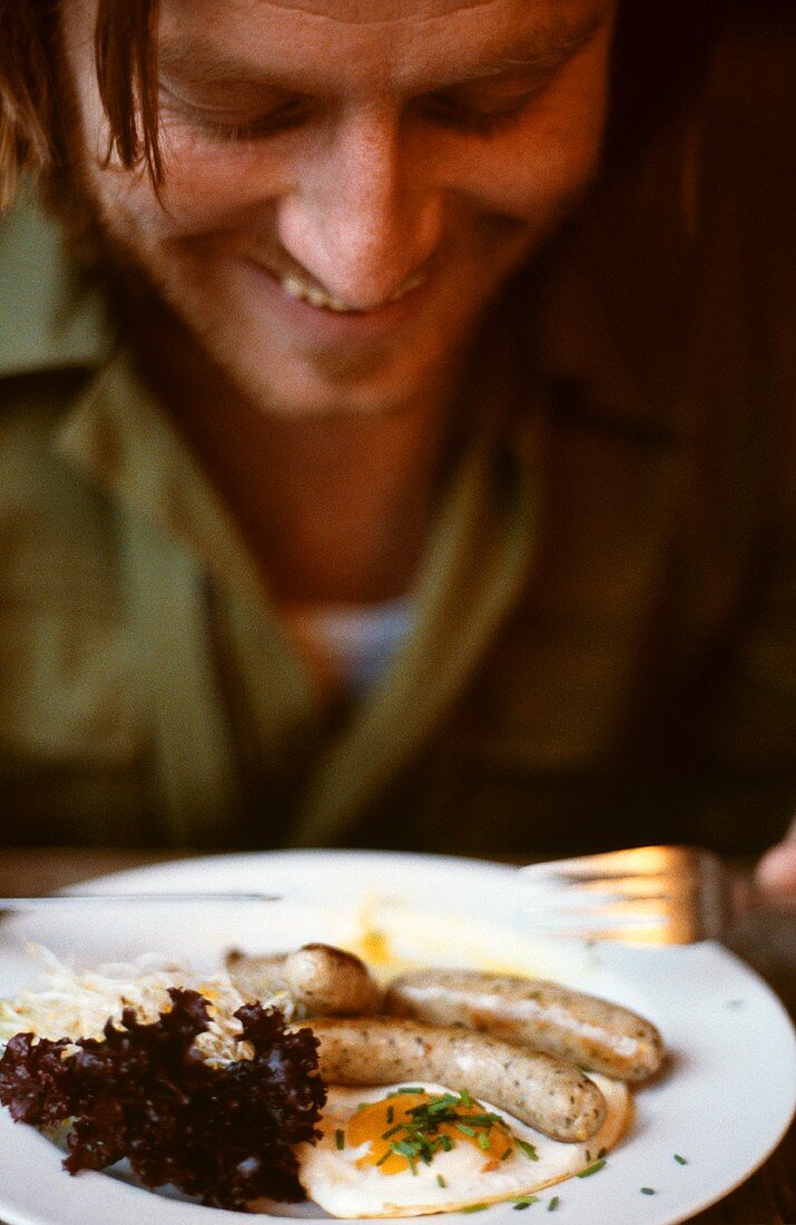 Man eating sausages with fried egg