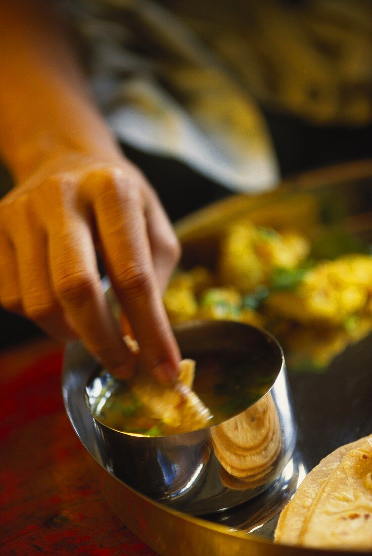 Hand dipping bread in curry sauce (India)