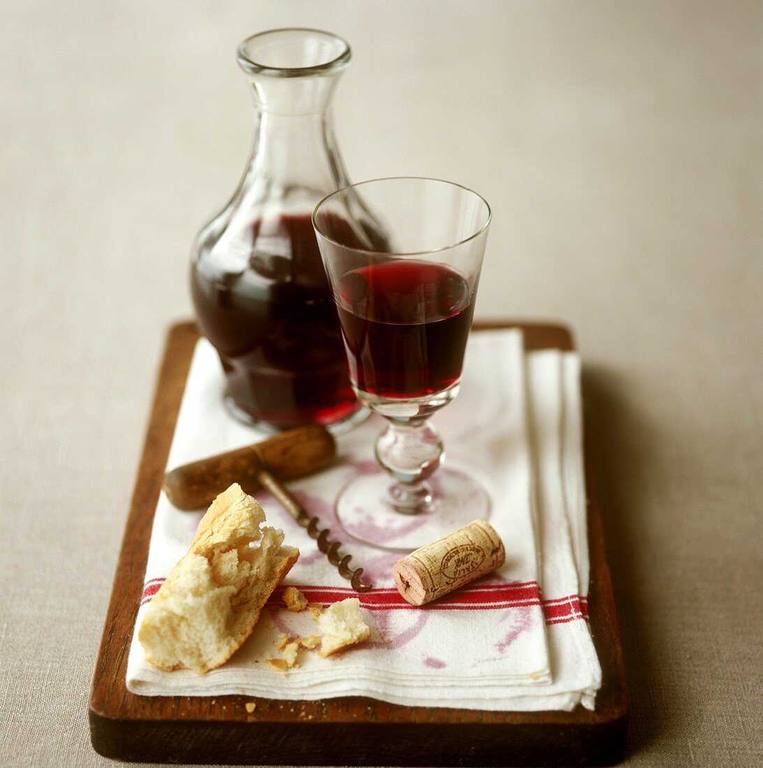 Glass of red wine with carafe, cork, corkscrew and white bread