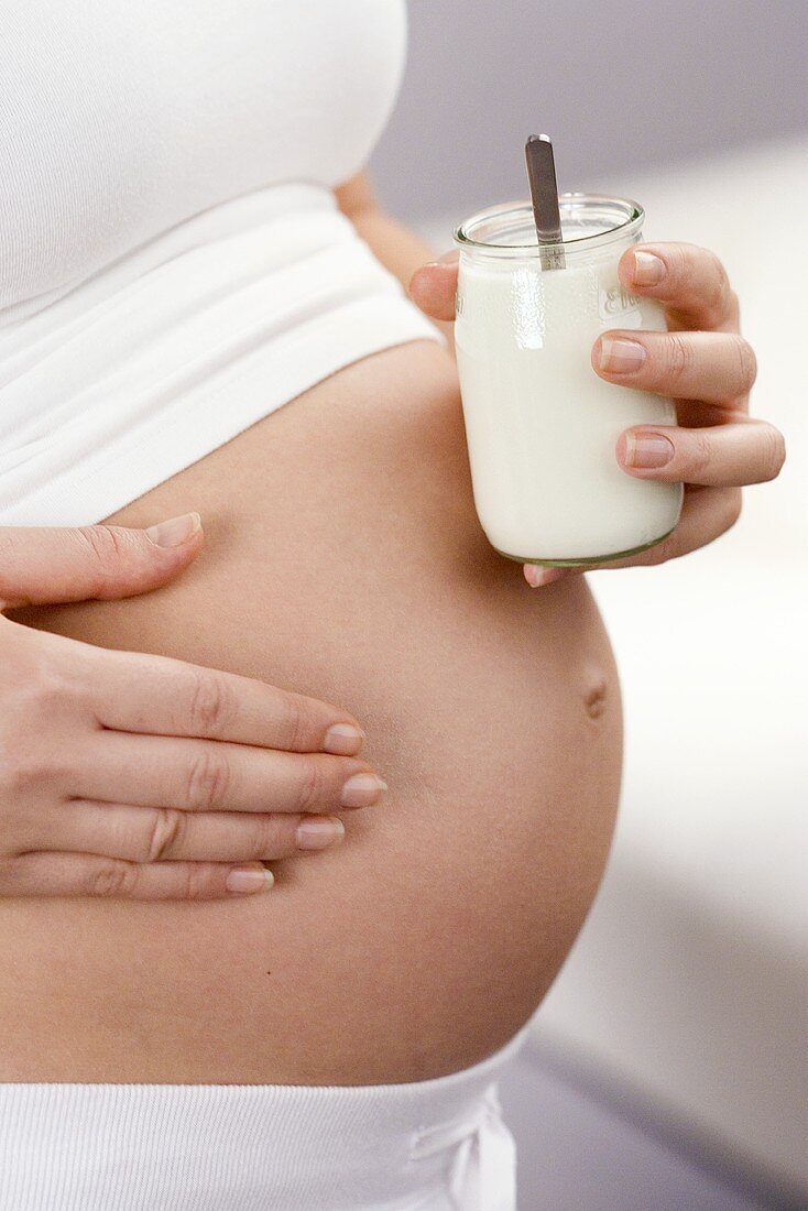 Pregnant woman with jar of yoghurt in front of stomach (detail)