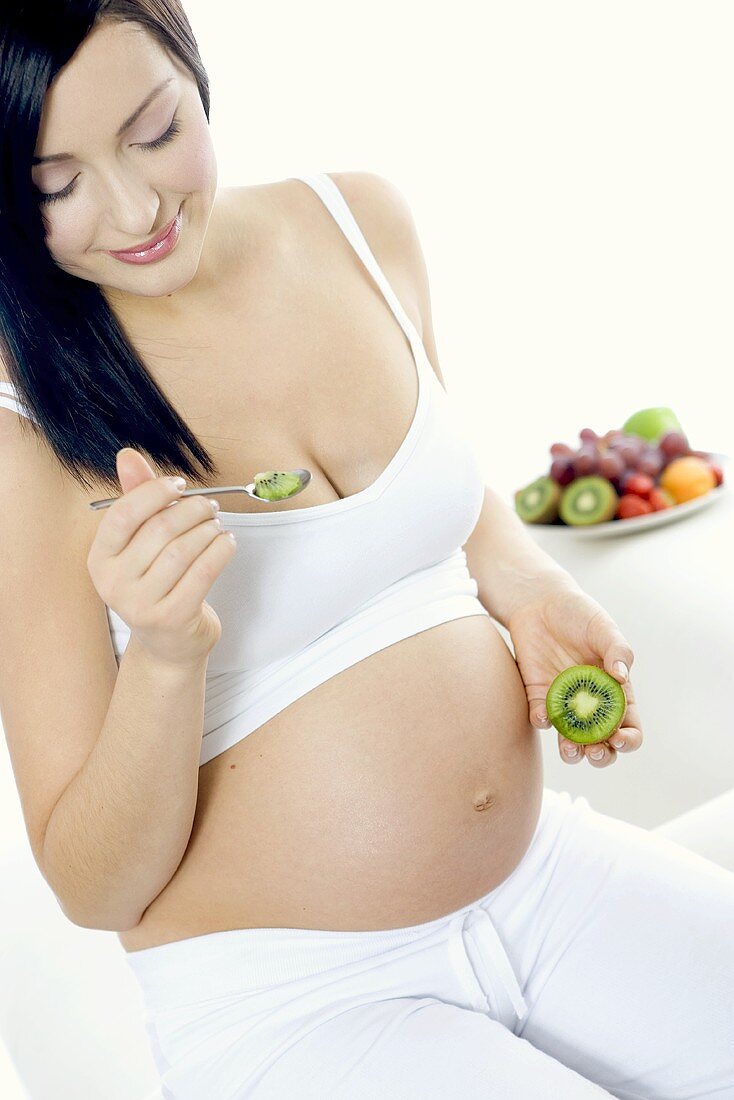 Pregnant woman seated, eating a kiwi fruit