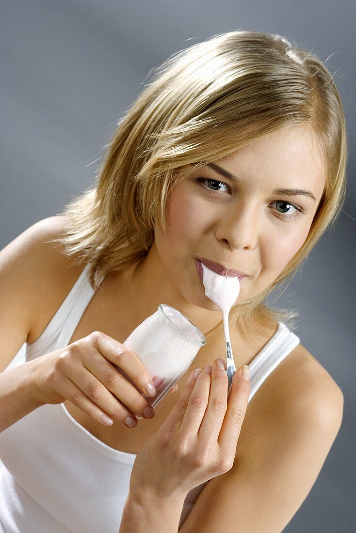 Junge Frau mit Joghurtglas, Löffel im Mund