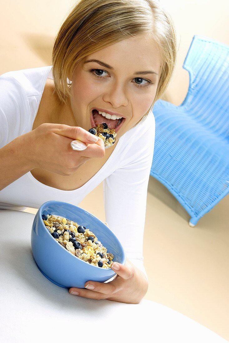 Junge Frau isst Müsli mit frischen Blaubeeren