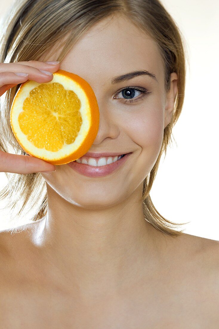 Young woman holding a slice of orange in front of her eye