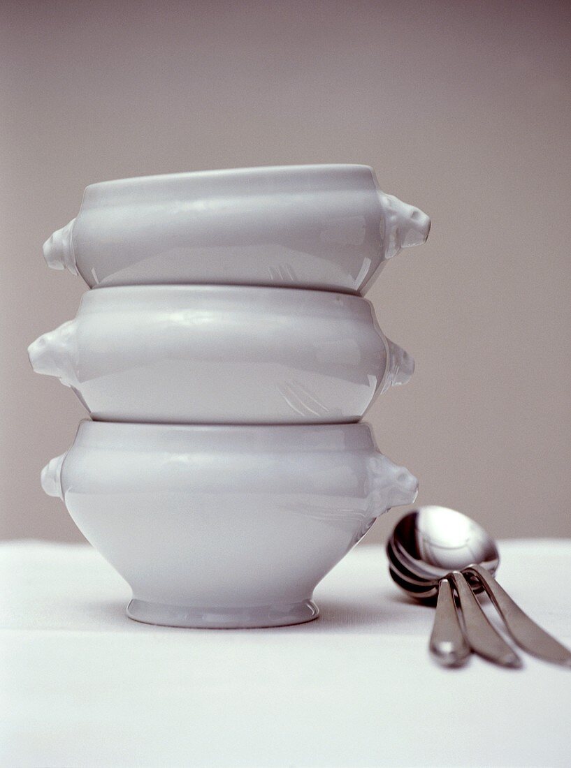 Three soup bowls in a pile with spoon beside them