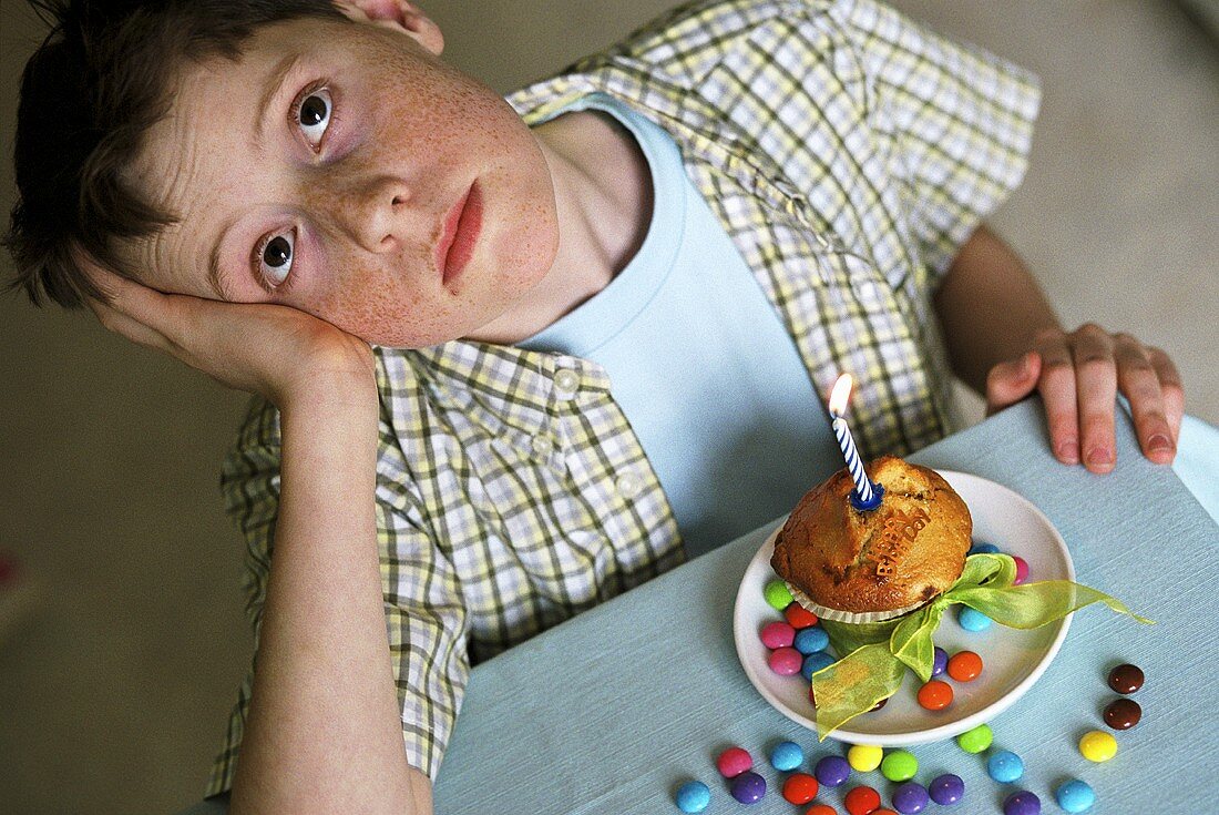 Boy sitting in front of birthday muffin, looking disappointed