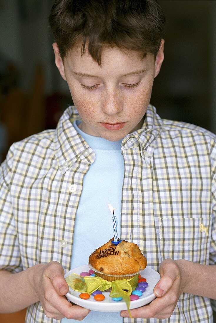 Junge hält Muffin mit brennender Kerze