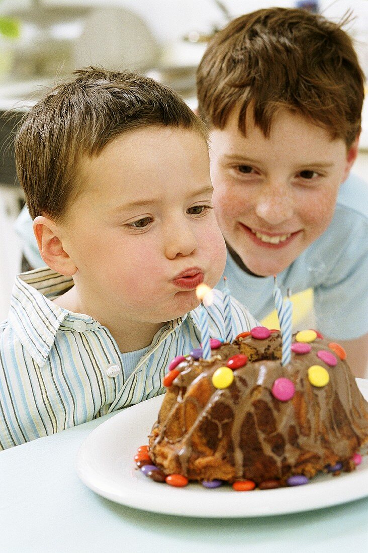 Junge bläst Geburtstagskerzen auf Kuchen aus