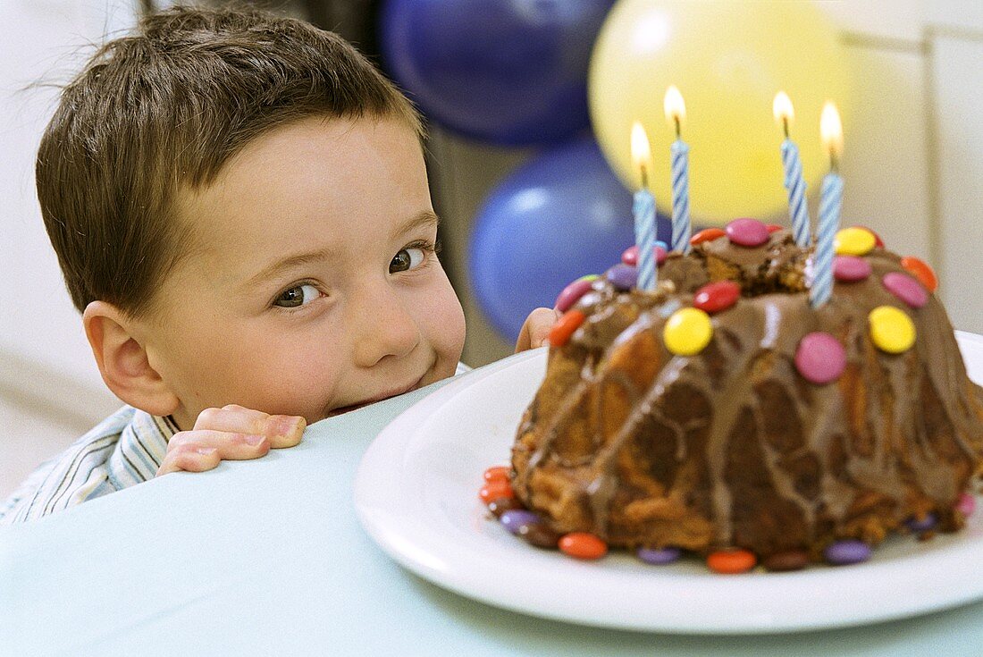 Mischievous boy peeping over table behind birthday cake