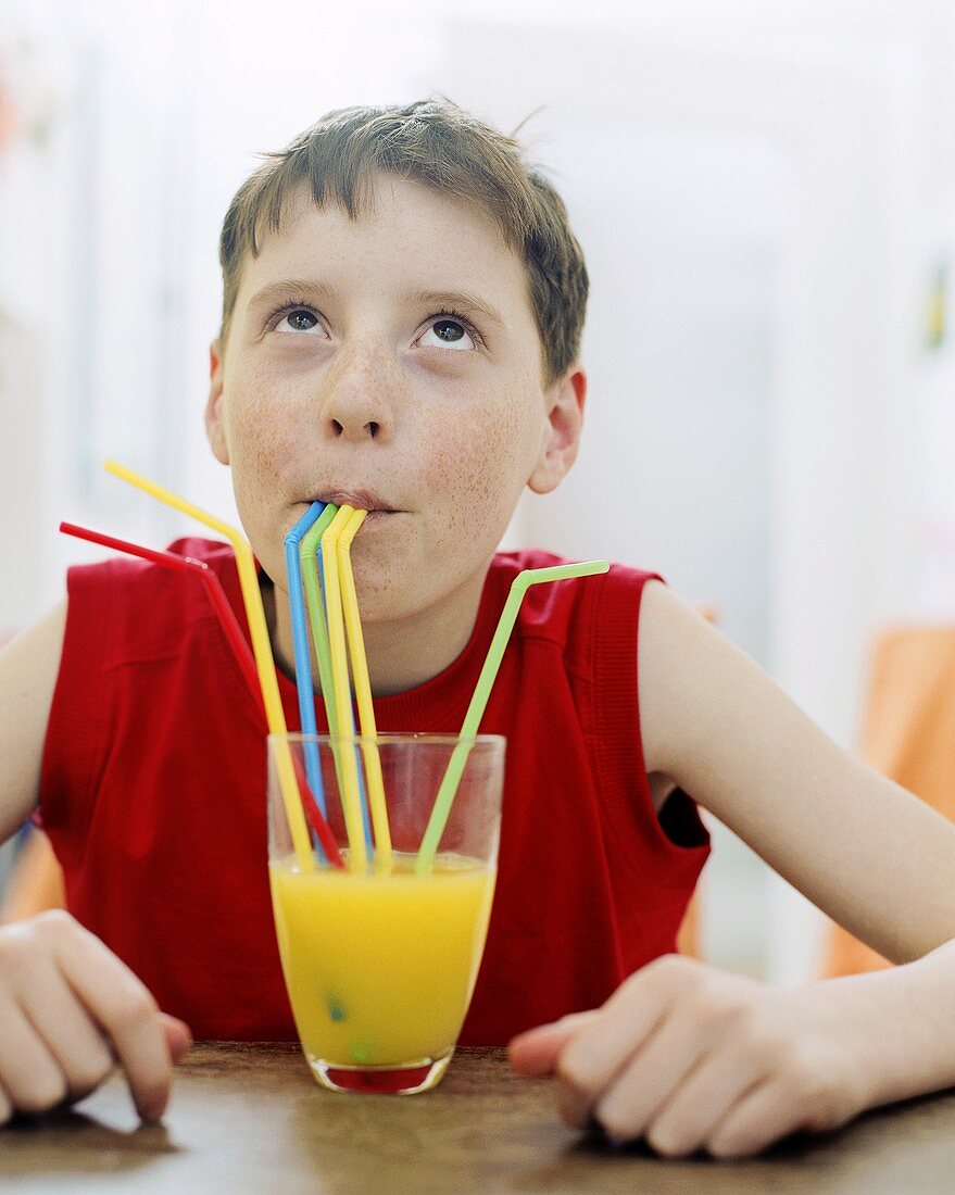 Junge trinkt Orangensaft mit vier Strohhalmen