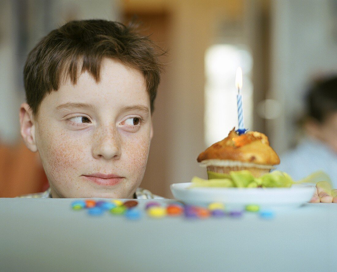 Junge blickt auf Muffin mit brenneder Kerze
