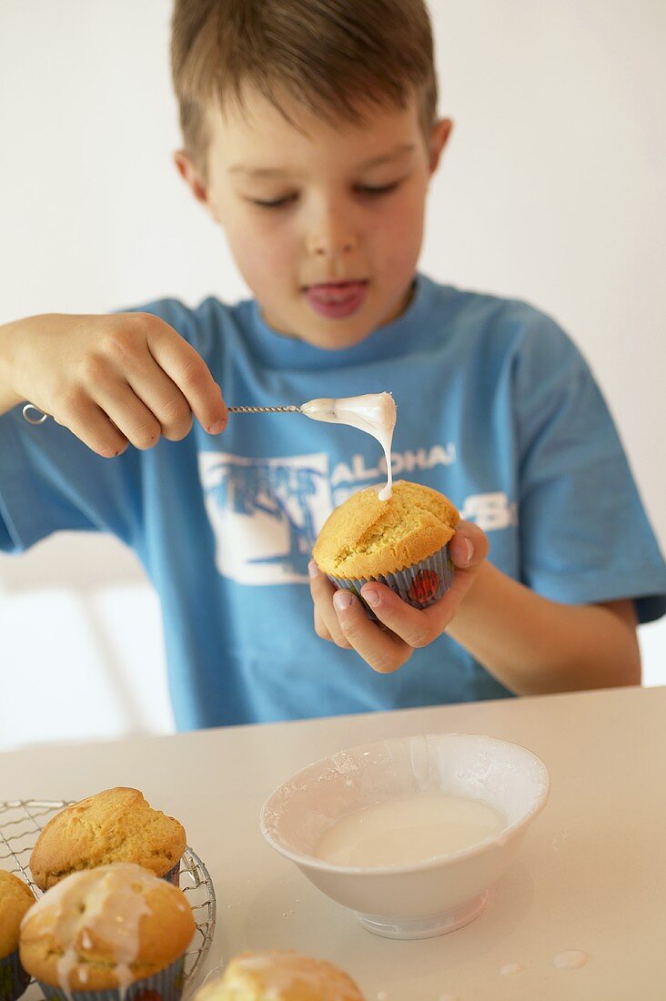 Junge bepinselt Muffin mit Zuckerglasur