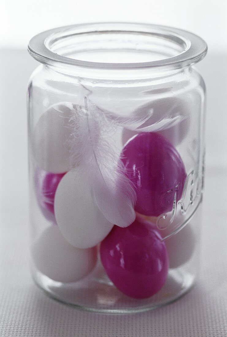Lila und weiße Eier mit Federn im Glas