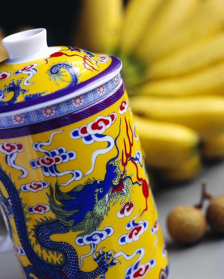 Teegefäss mit chinesischem Motiv, im Hintergrund Bananen