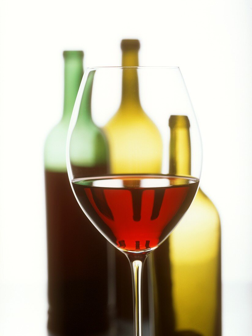 Glas Rotwein vor drei Weinflaschen