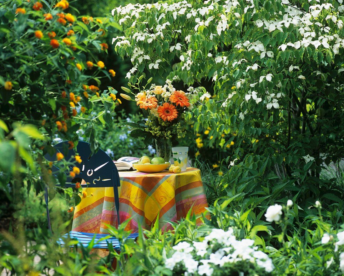 Fruit bowl, flowers & book on table in flower-filled garden