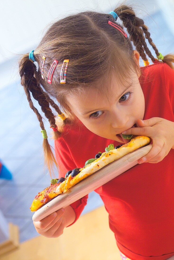 Small girl hungrily eating a vegetable pizza 