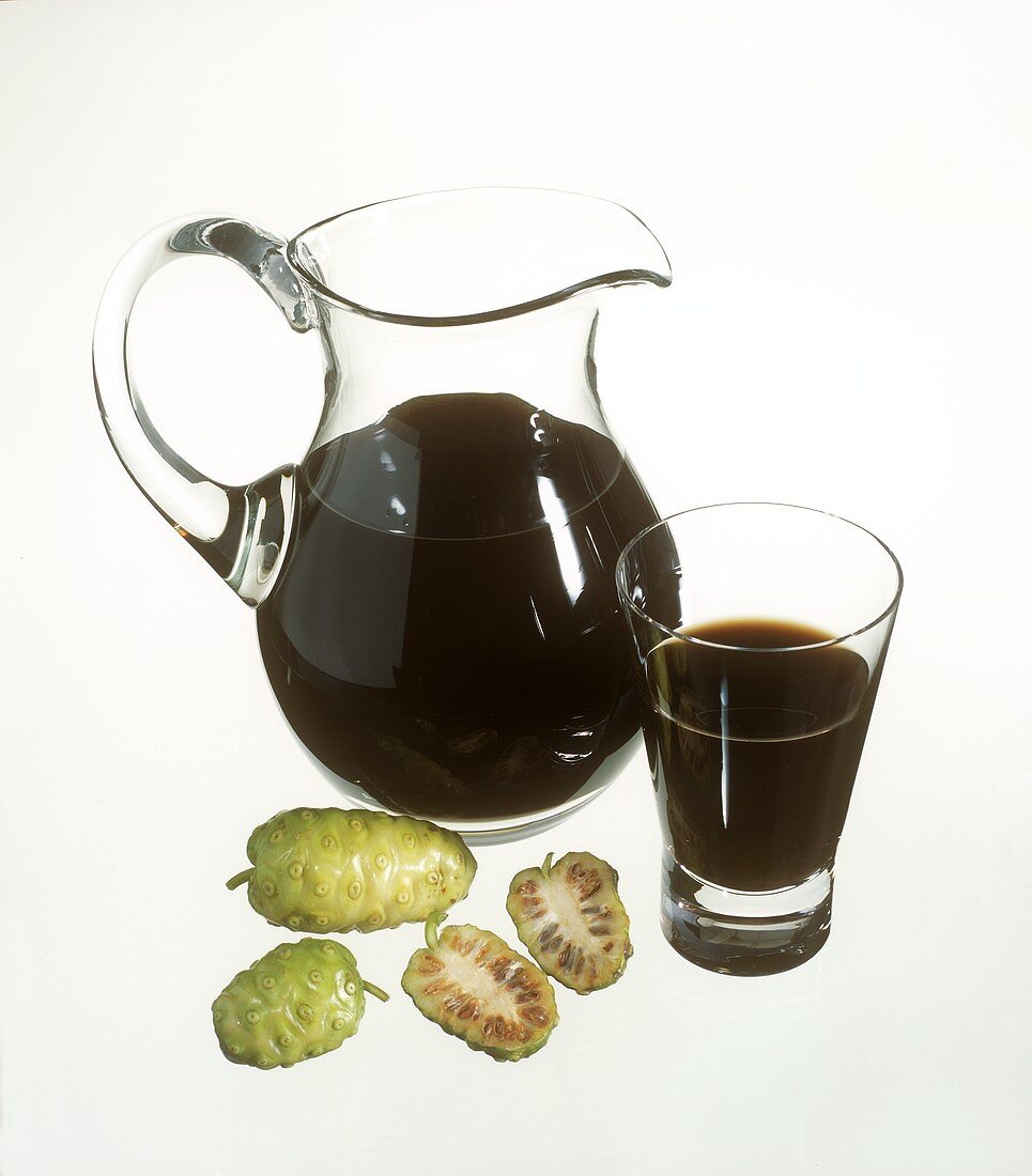 Noni juice in carafe and glass, noni fruits in front