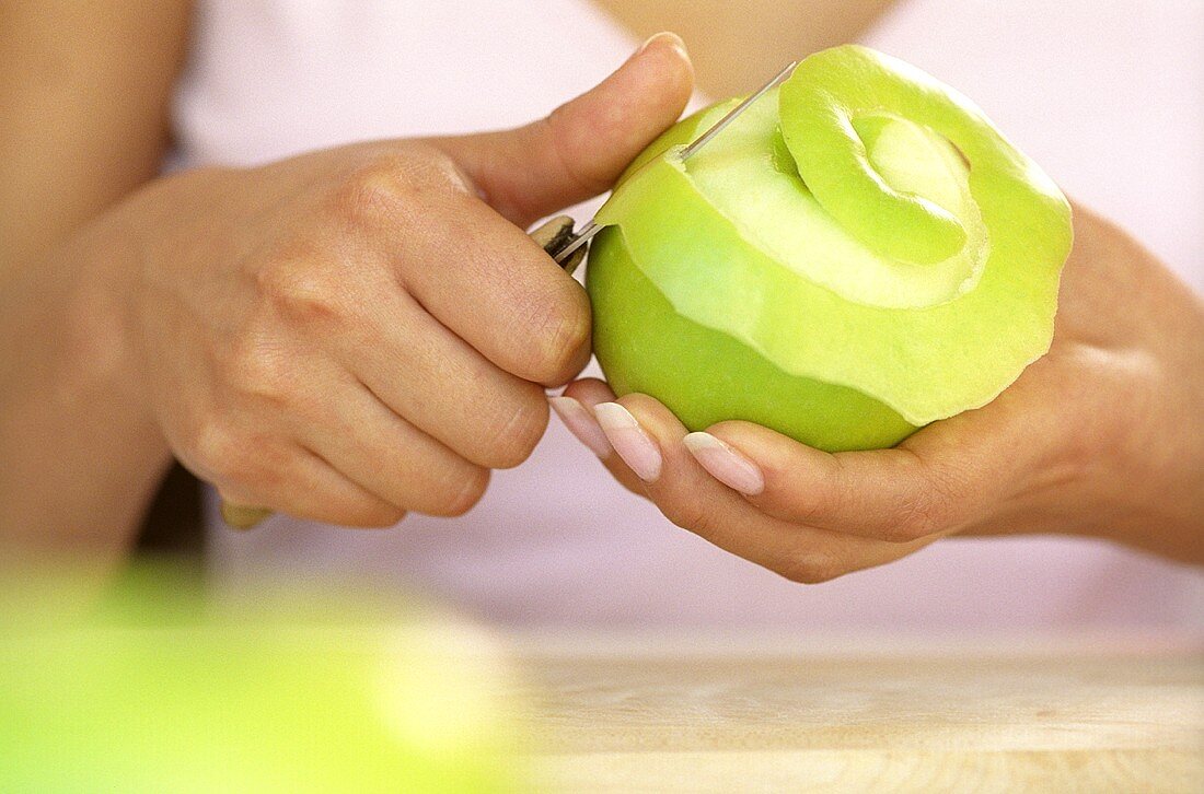 Hands peeling a green apple