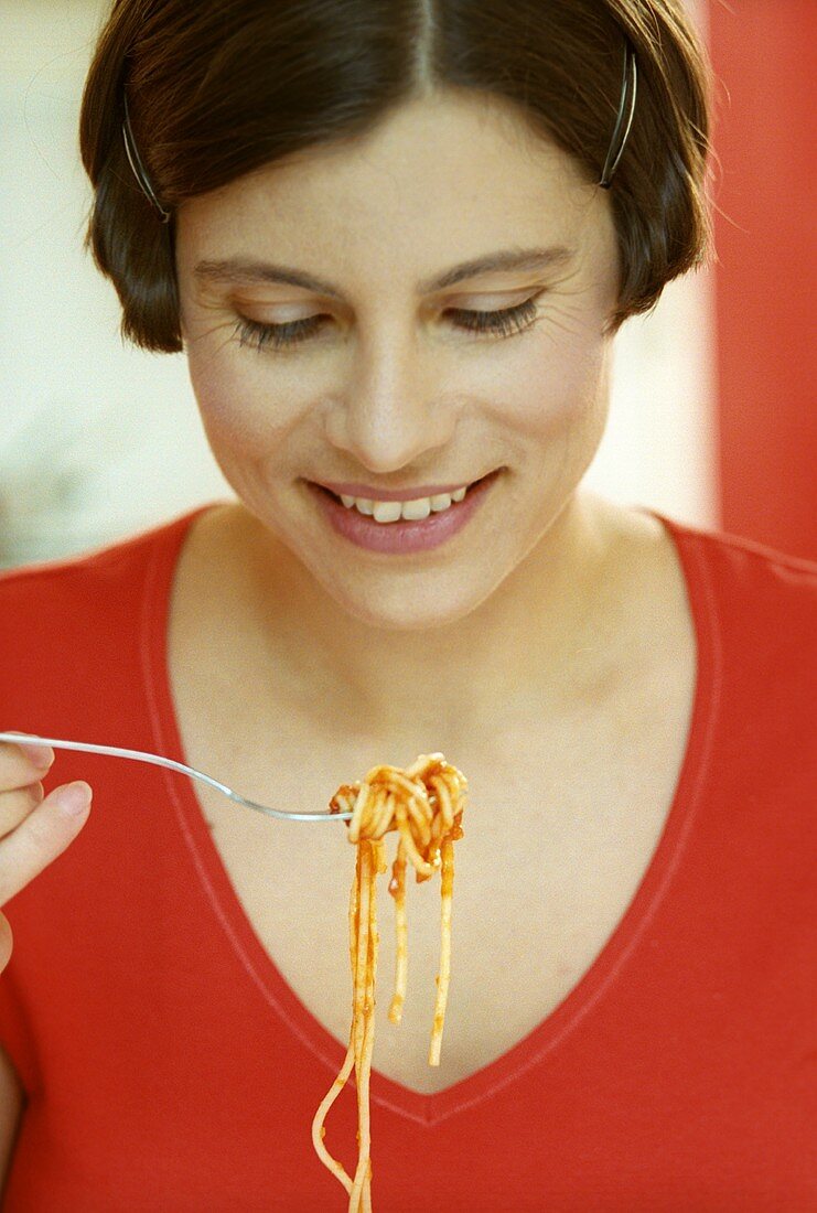 Woman holding forkful of spaghetti and tomato sauce