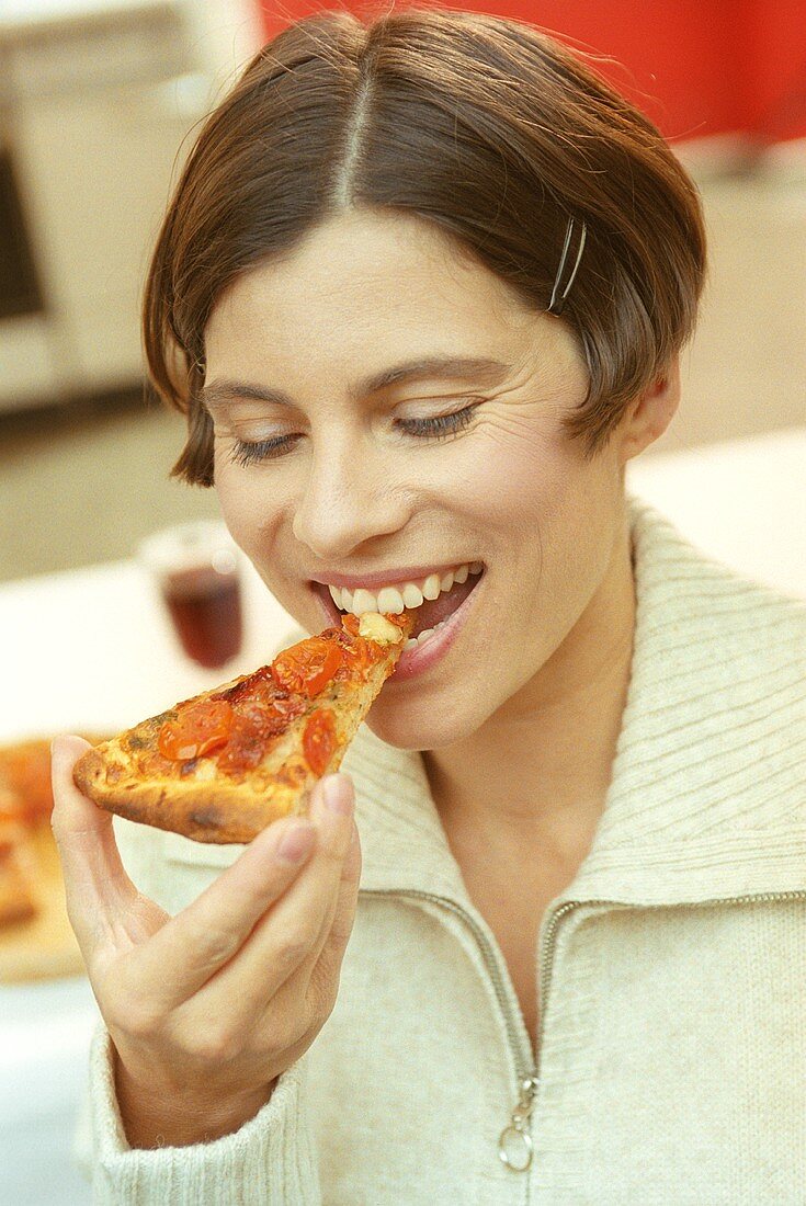 Junge Frau beisst in ein Stück Pizza