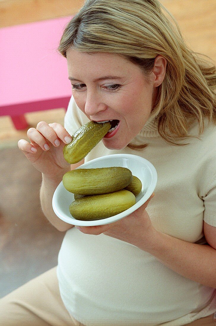 Pregnant woman biting into gherkin (grainy effect)