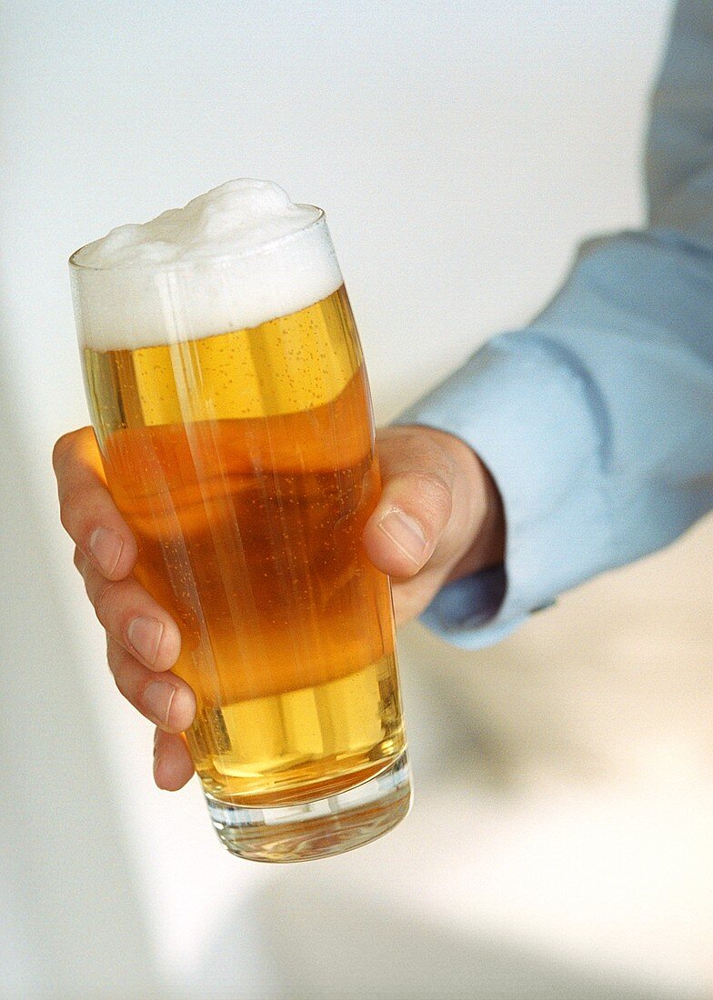 Hand hält Glas helles Bier