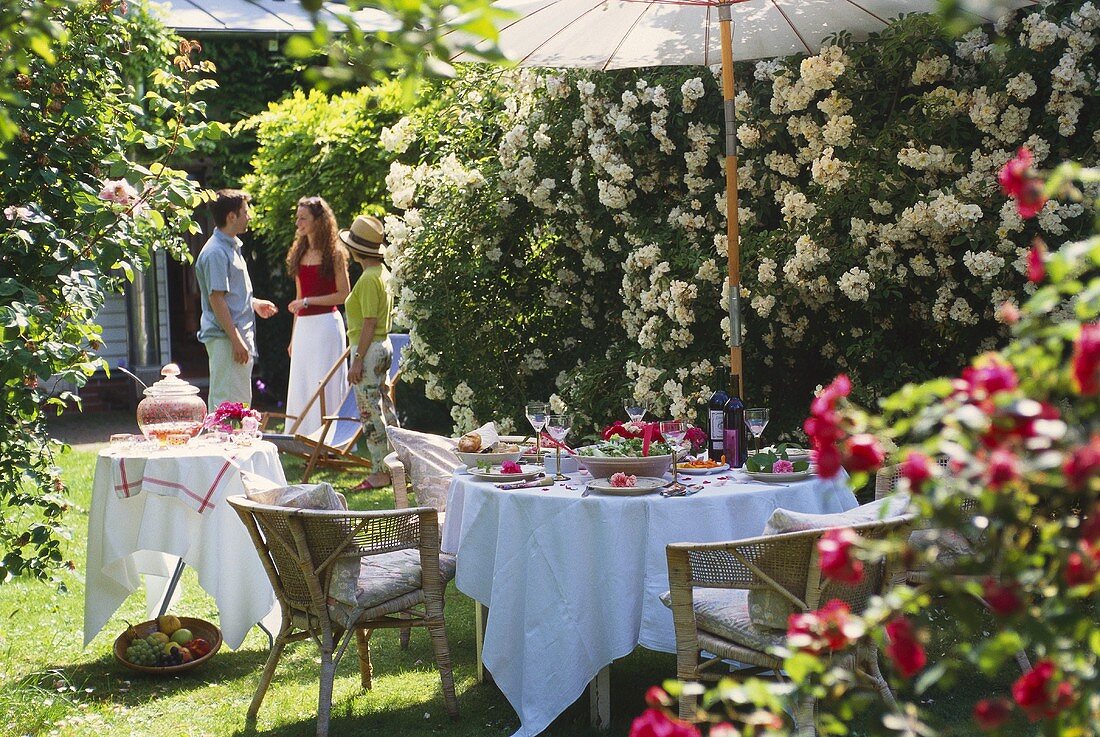 Festlich gedeckter Gartentisch vor weissen Rosenkaskaden