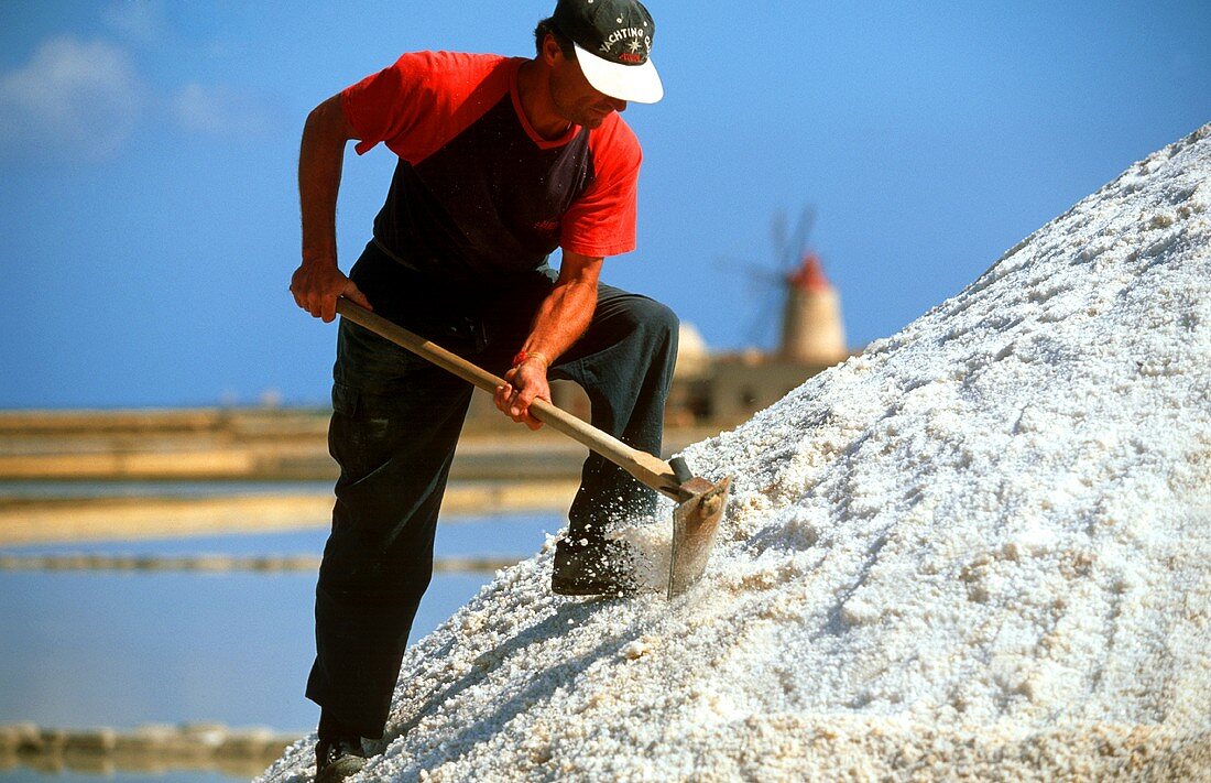 Man working on salt mountain; salt pans near Trapani, Italy