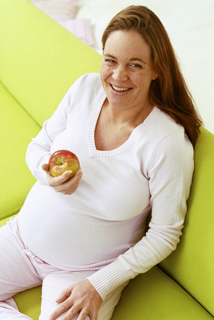 Schwangere Frau auf dem Sofa isst einen Apfel