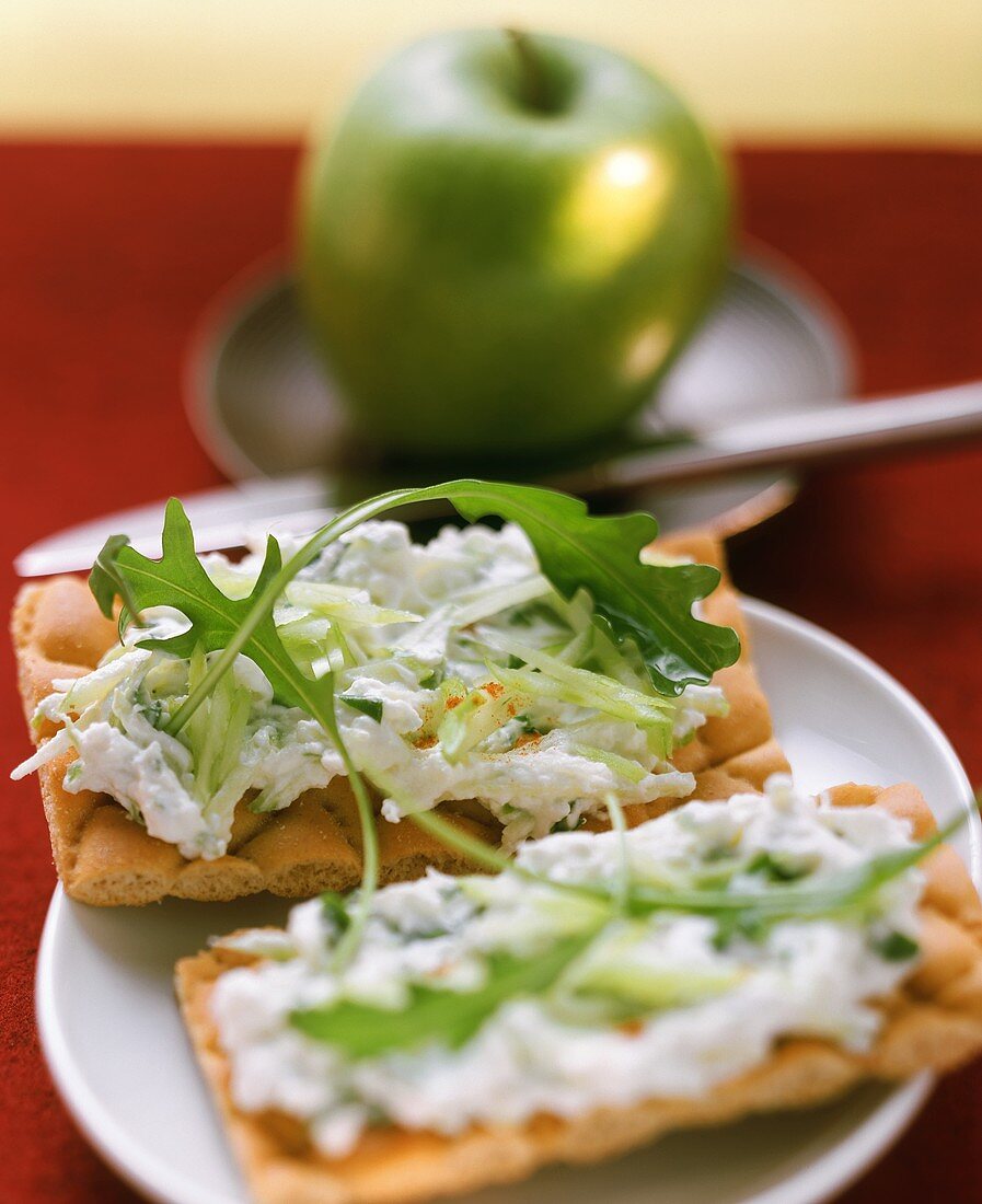 Mit Quark und Rucola belegtes Knäckebrot und ein Apfel