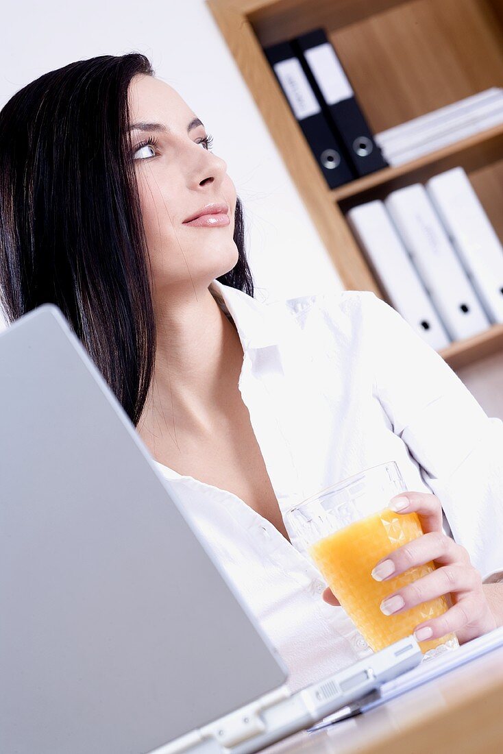 Junge Frau sitzt im Büro mit einem Glas Orangensaft