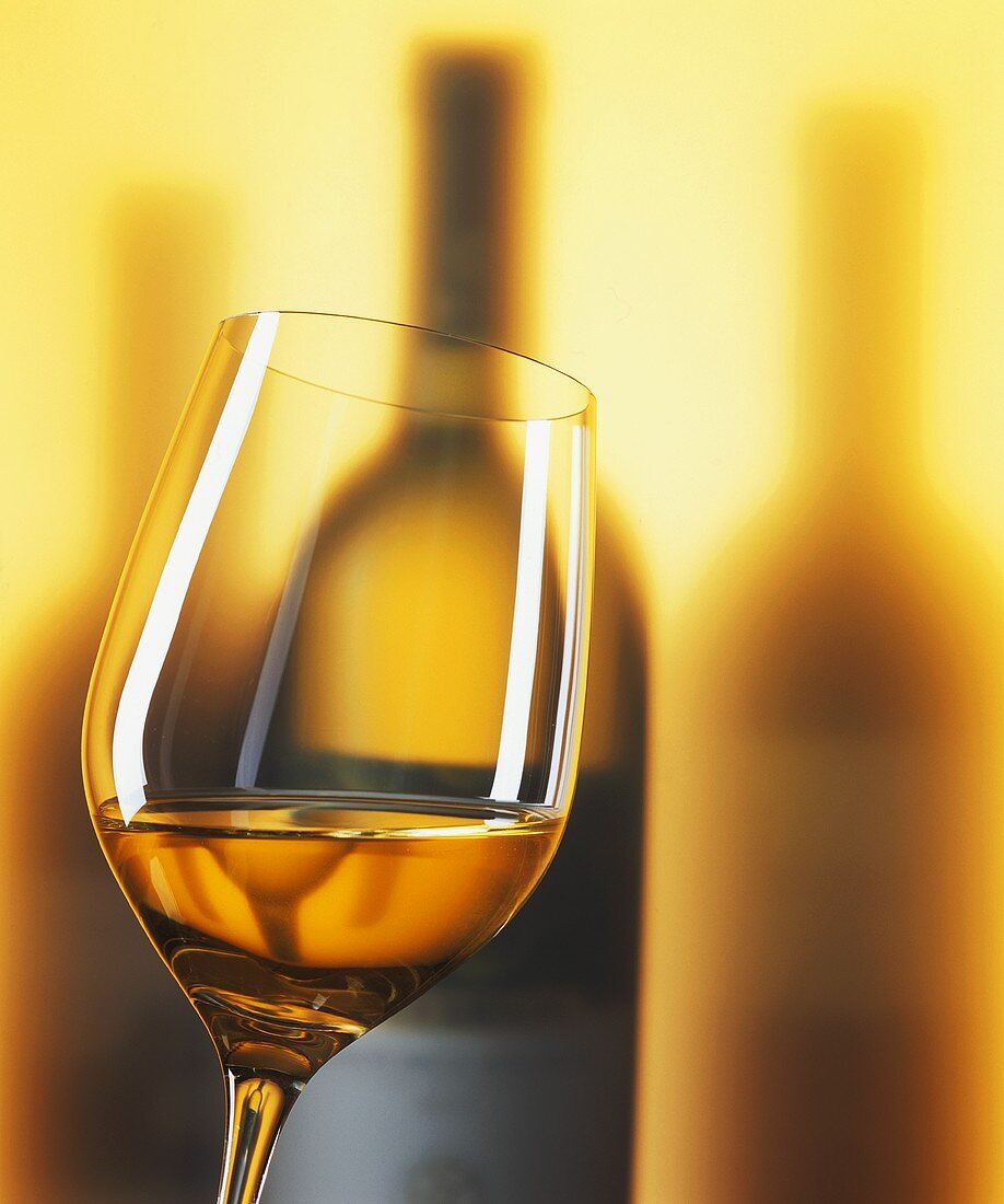 A glass of white wine with wine bottles in background