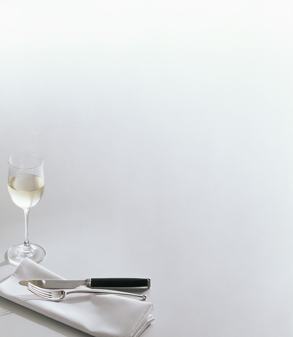 Silver cutlery on napkin and white wine glass