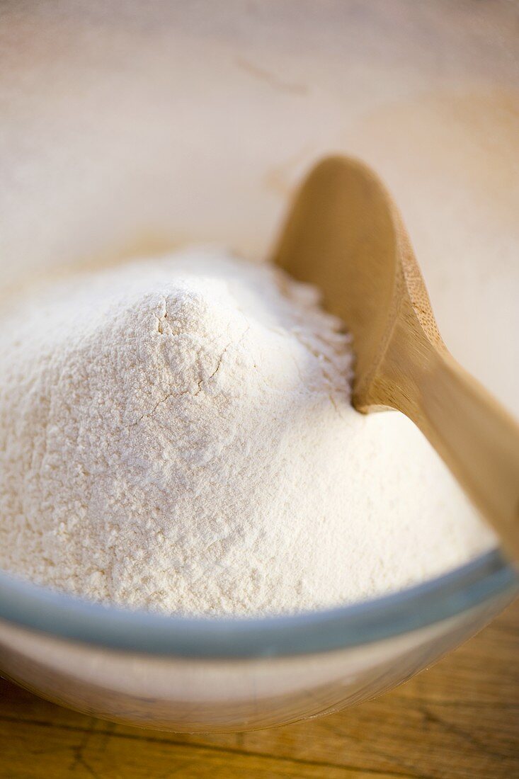Flour in a small glass bowl with wooden spoon