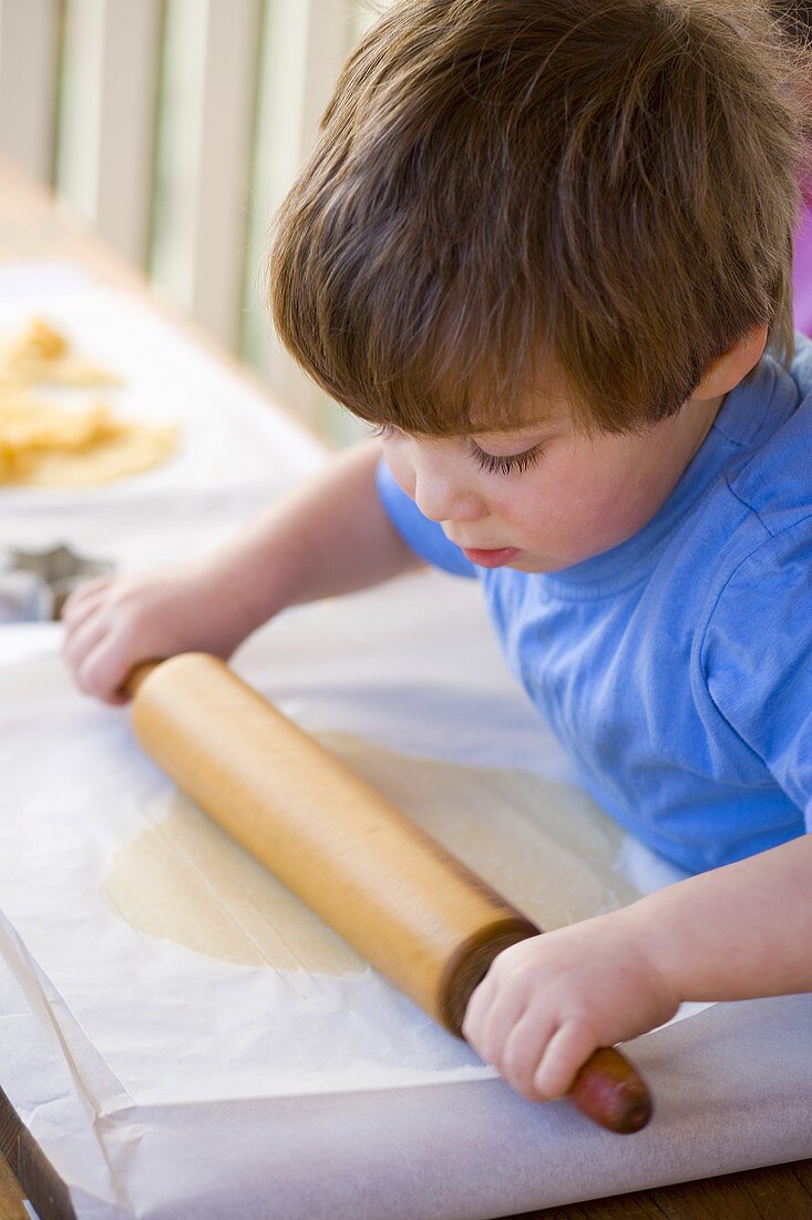 Kleiner Junge rollt Plätzchenteig zwischen Butterpapier aus