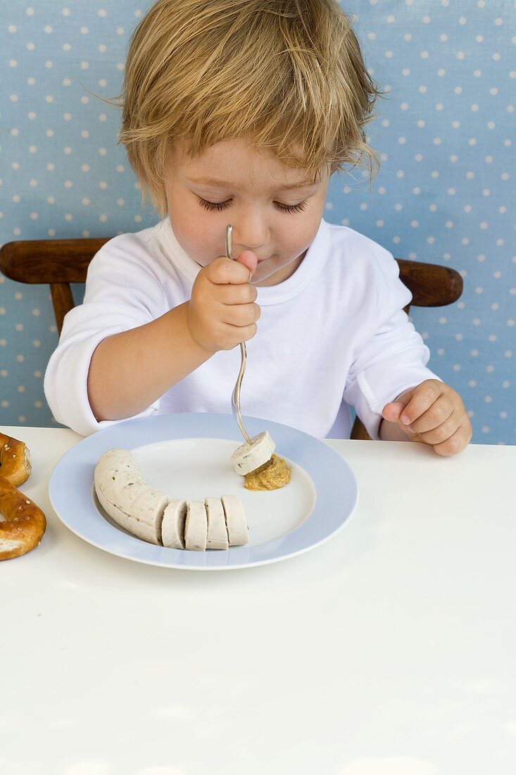 Kleiner Junge isst eine Weisswurst